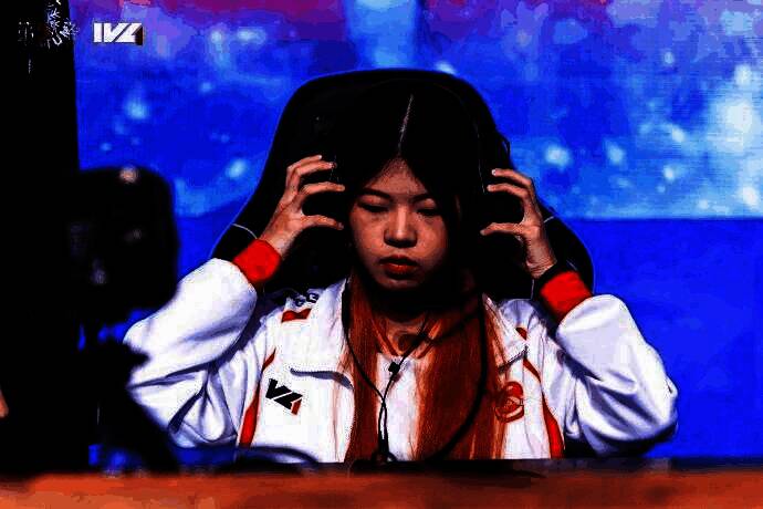 GG_violet选手专注比赛中的特写镜头，眼神坚定，耳机微斜，背景为赛事现场灯光与屏幕画面