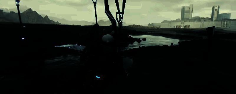 《死亡搁浅2》中主角手持消音狙击枪潜伏于山地环境，枪身细节清晰，背景为荒凉废土与远处敌人哨岗