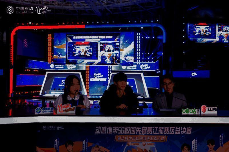 傲寒与景晚在解说台前激情解说，身旁是大屏幕上的比赛画面，现场观众热烈鼓掌