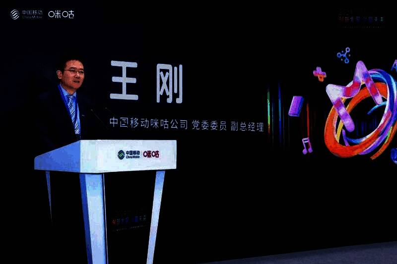 王刚在台上发表讲话,身后大屏展示咪咕云游戏战略布局图,包含技术架构与生态合作模式